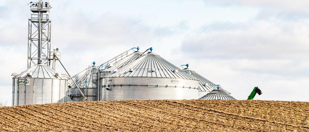 Grain bins in the background and harvested field in the foreground, under partly cloudy sky 